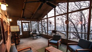 Ein gemütliches Zimmer mit Holzbalkendecke, großen Fenstern, einem Tisch mit Stühlen und einer Bank.