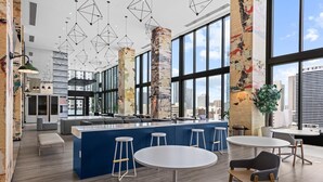 A modern interior with a central bar area, high ceilings, and large windows offering city views.