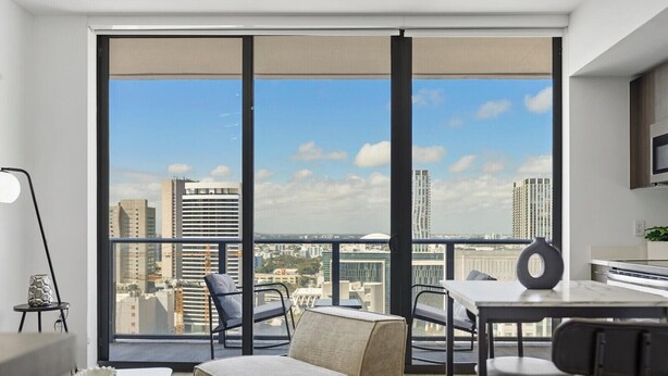 A modern living room with a large window, a sofa, a dining table, and chairs.
