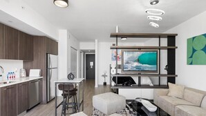 A modern apartment with a kitchen, dining area, and living room. It includes a flat-screen TV, a sofa, a coffee table, and a TV stand.