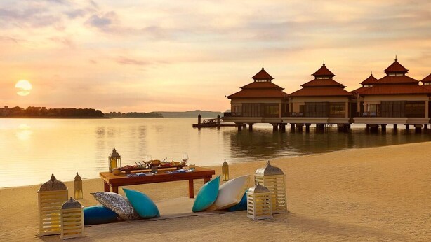 A serene lakeside setting with overwater bungalows, a dining setup with a table and chairs, and a sunset view. - Luxury 1- Bedroom at Anantara Palm Jumeirah (Dubai)