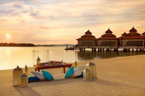 A serene lakeside setting with overwater bungalows, a dining setup with a table and chairs, and a sunset view. - Luxury 1- Bedroom at Anantara Palm Jumeirah (Dubai)
