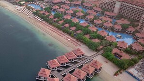 An aerial view of a resort with multiple overwater bungalows, a beach, and a large building with a red roof. - Luxury 1- Bedroom at Anantara Palm Jumeirah (Dubai)