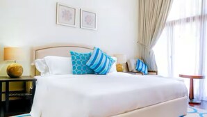 A neatly made bed with a white comforter and blue patterned pillows, a bedside table with a lamp, and a framed picture on the wall. - Luxury 1- Bedroom at Anantara Palm Jumeirah (Dubai)