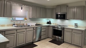 A modern kitchen with grey cabinets, stainless steel appliances, and a tiled floor. - Multi Family House 4Bed/3Bath-Large Fenced Yard with Activities for Whole Family (Fruitland Park)