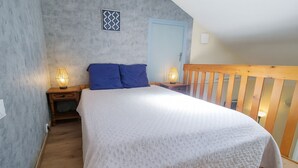 A bedroom with a large bed, two nightstands, a wooden railing, and a door.