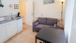 A compact living space with a kitchenette, a sofa, a table, and a painting on the wall.