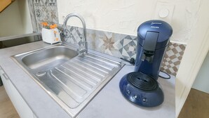 A kitchen with a stainless steel sink, a coffee maker, and a fruit bowl with oranges.