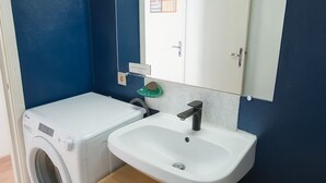 A compact bathroom with a washing machine, a sink, and a mirror.