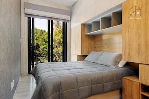Un dormitorio moderno con una cama grande, cabecera de madera integrada y vistas a árboles a través de una puerta corrediza.