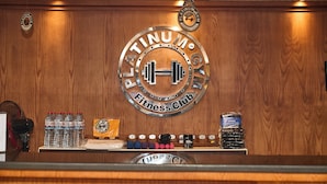 A Platinum Fitness Club sign with a wooden wall background, water bottles, dumbbells, and a fan. - The Fit Stop Hostel (Hurghada)