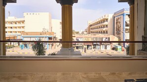 A view from a balcony with a central column, overlooking a street with buildings, including a shopping center and a store named "Kaufland Shopping C". - The Fit Stop Hostel (Hurghada)