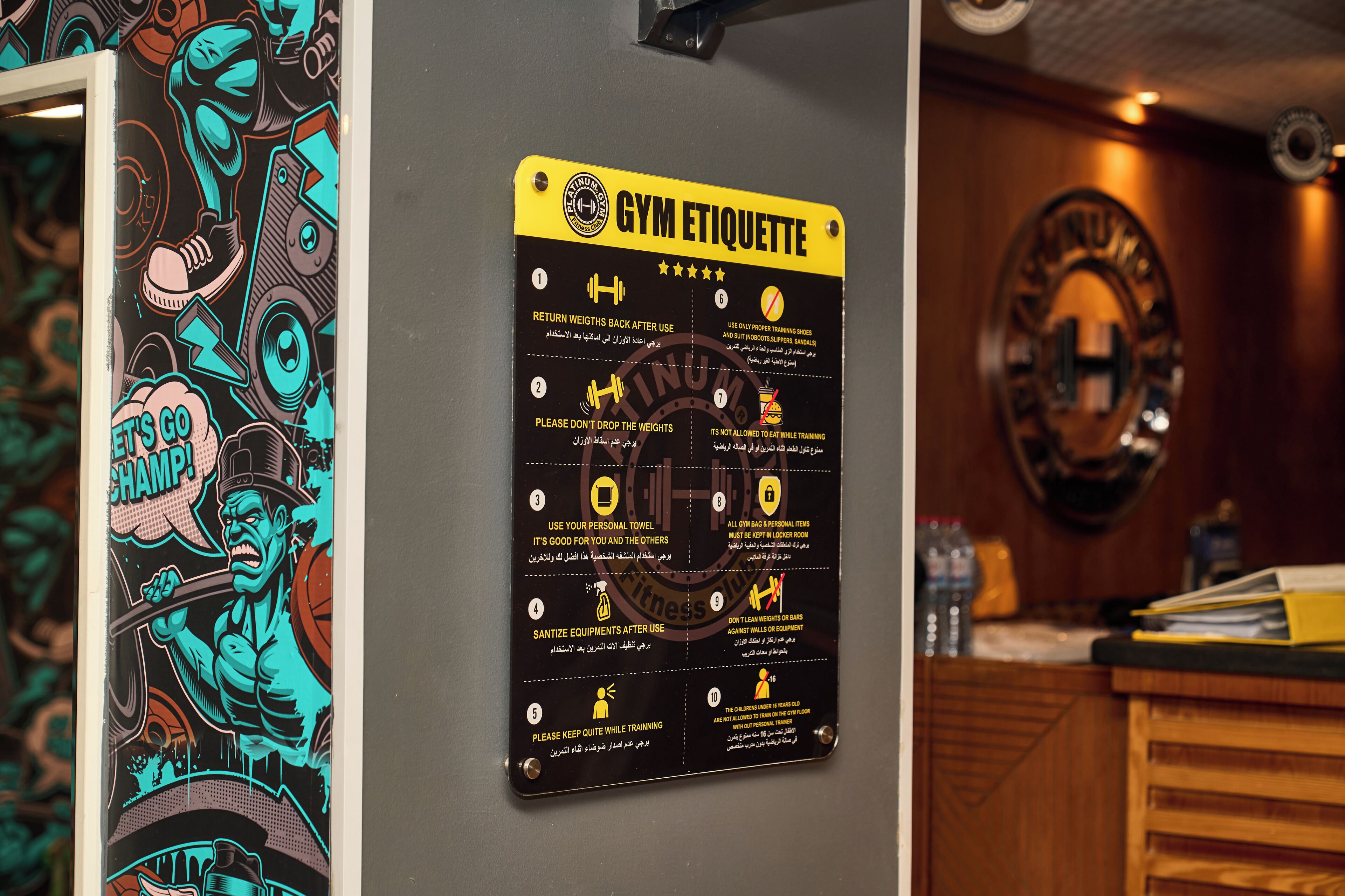 A gym etiquette poster on a wall with a mirror and a wooden counter.