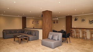 A modern living room with a sectional sofa, a small armchair, a coffee table, and a bar area with stools. - The Fit Stop Hostel (Hurghada)