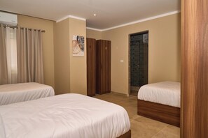 A hotel room with two single beds, a wooden wardrobe, a bathroom with a shower, and a wall-mounted air conditioner. - The Fit Stop Hostel (Hurghada)