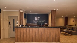 A reception area with a wooden reception desk, a large screen displaying 'The Fit House' logo, a digital clock, and a reception counter. - The Fit Stop Hostel (Hurghada)