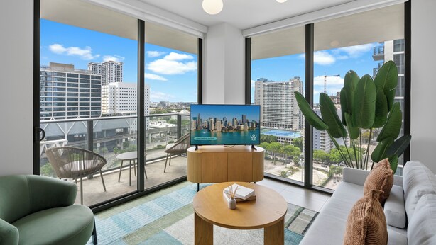 Ein modernes Wohnzimmer mit Fernseher, einer Couch, einem runden Tisch und einem Balkon mit Blick auf die Stadt.