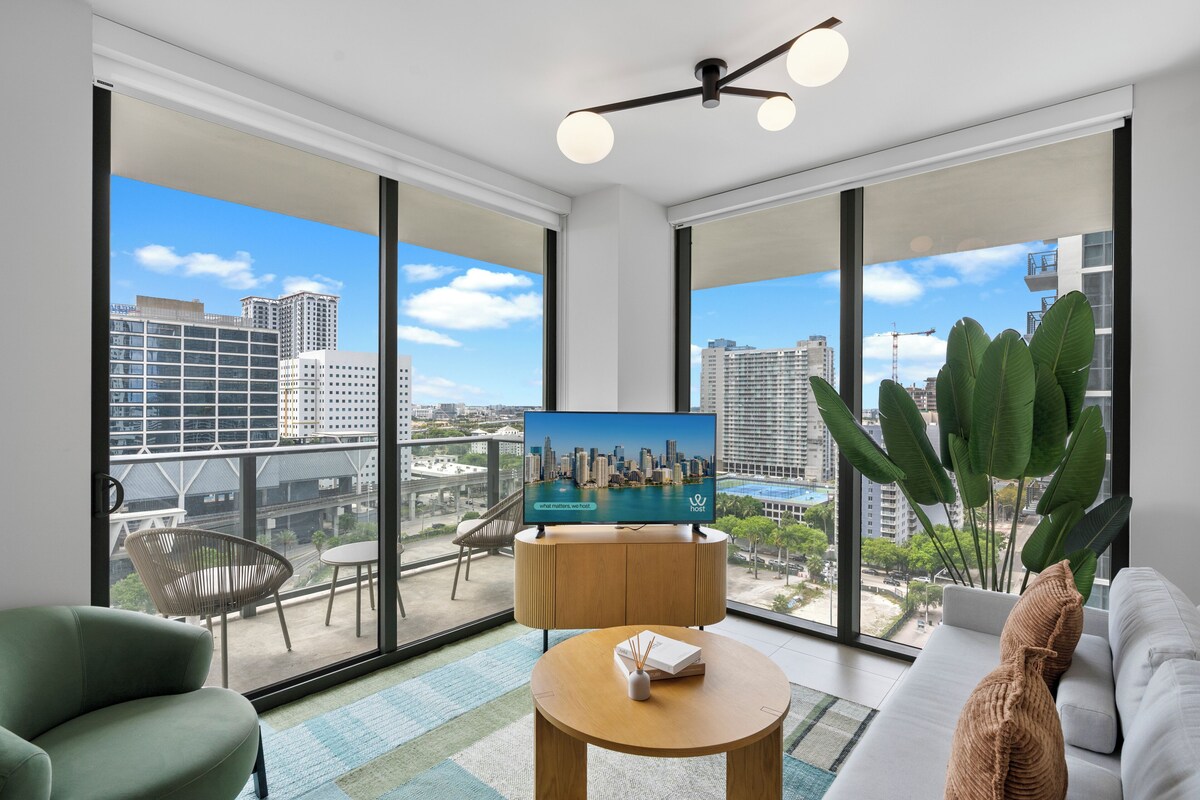 Ein modernes Wohnzimmer mit Fernseher, einer Couch, einem runden Tisch und einem Balkon mit Blick auf die Stadt.