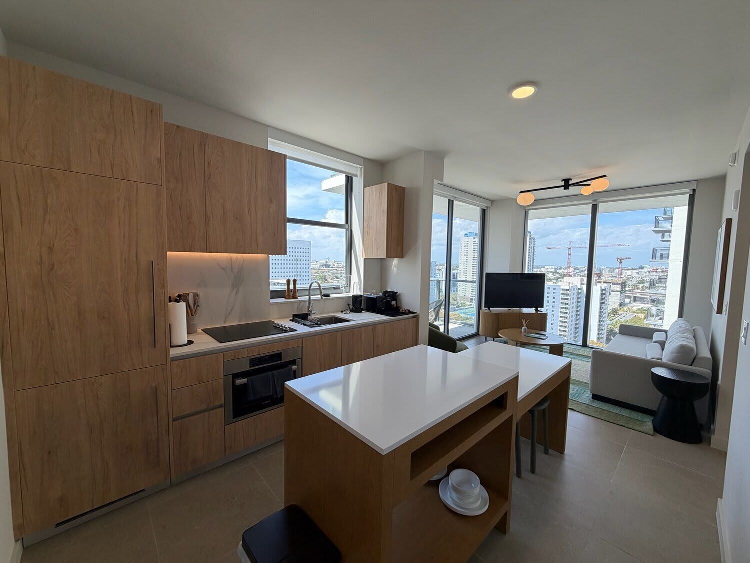 A modern kitchen with wooden cabinets, a built-in oven, and a large window offering a city view.