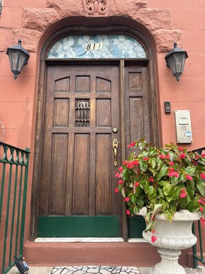 A wooden door with a glass panel and the number 811, a green door mat, and a potted plant with red flowers.