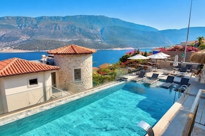 A clear blue pool with a stone building and lounge chairs, overlooking a mountainous coastline. - Adasya Hotel (Kas)