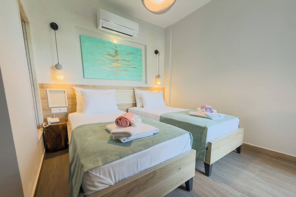 Habitación de hotel con dos camas, aire acondicionado de pared, un cuadro y una mesita de noche con lámpara.