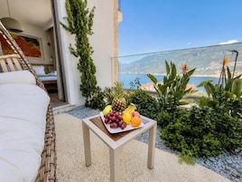 Un balcón con una mesa llena de fruta, un sofá de mimbre y vistas al mar.