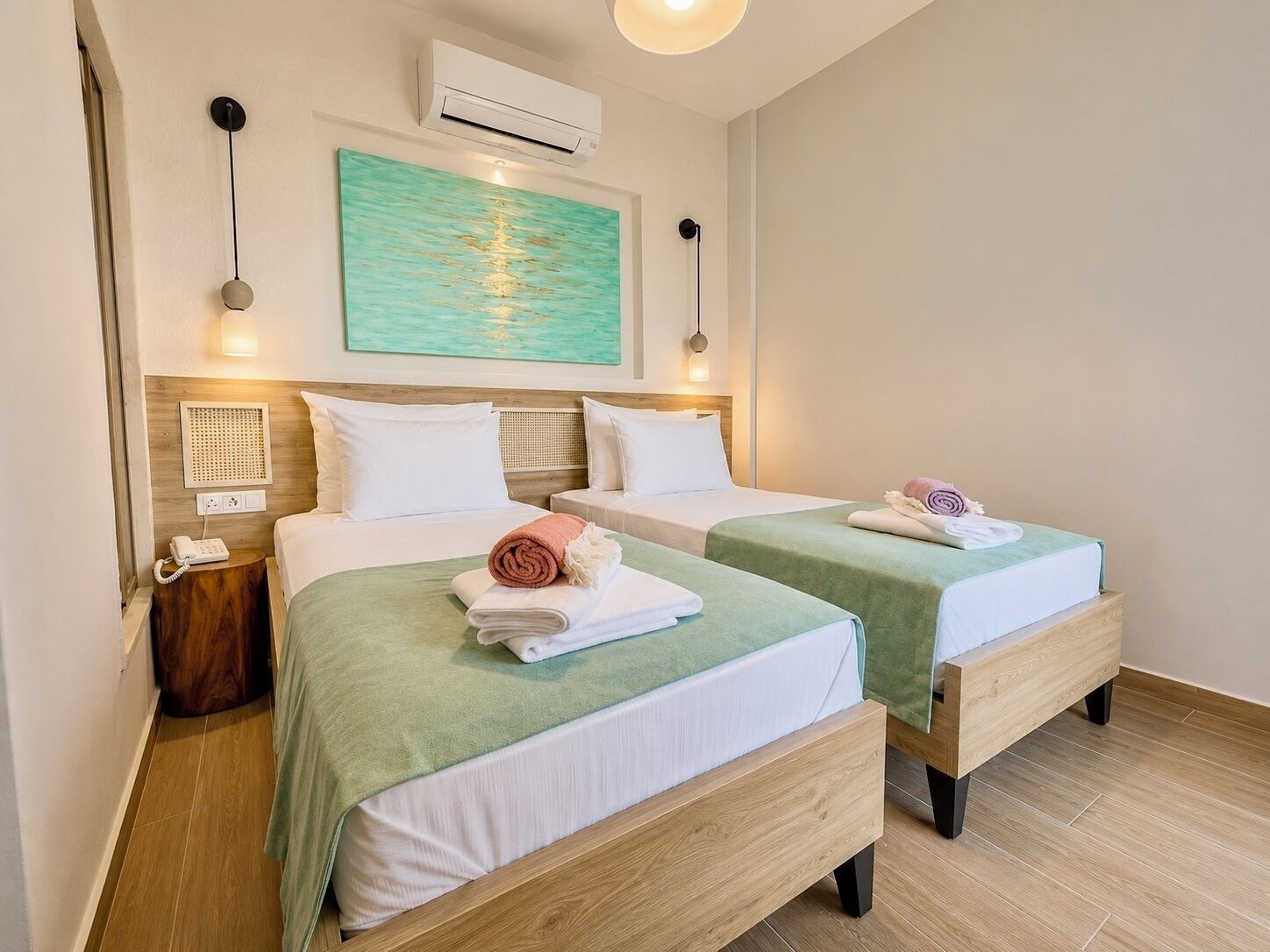 A hotel room with two beds, a painting, an air conditioner, a bedside telephone, and a small table.