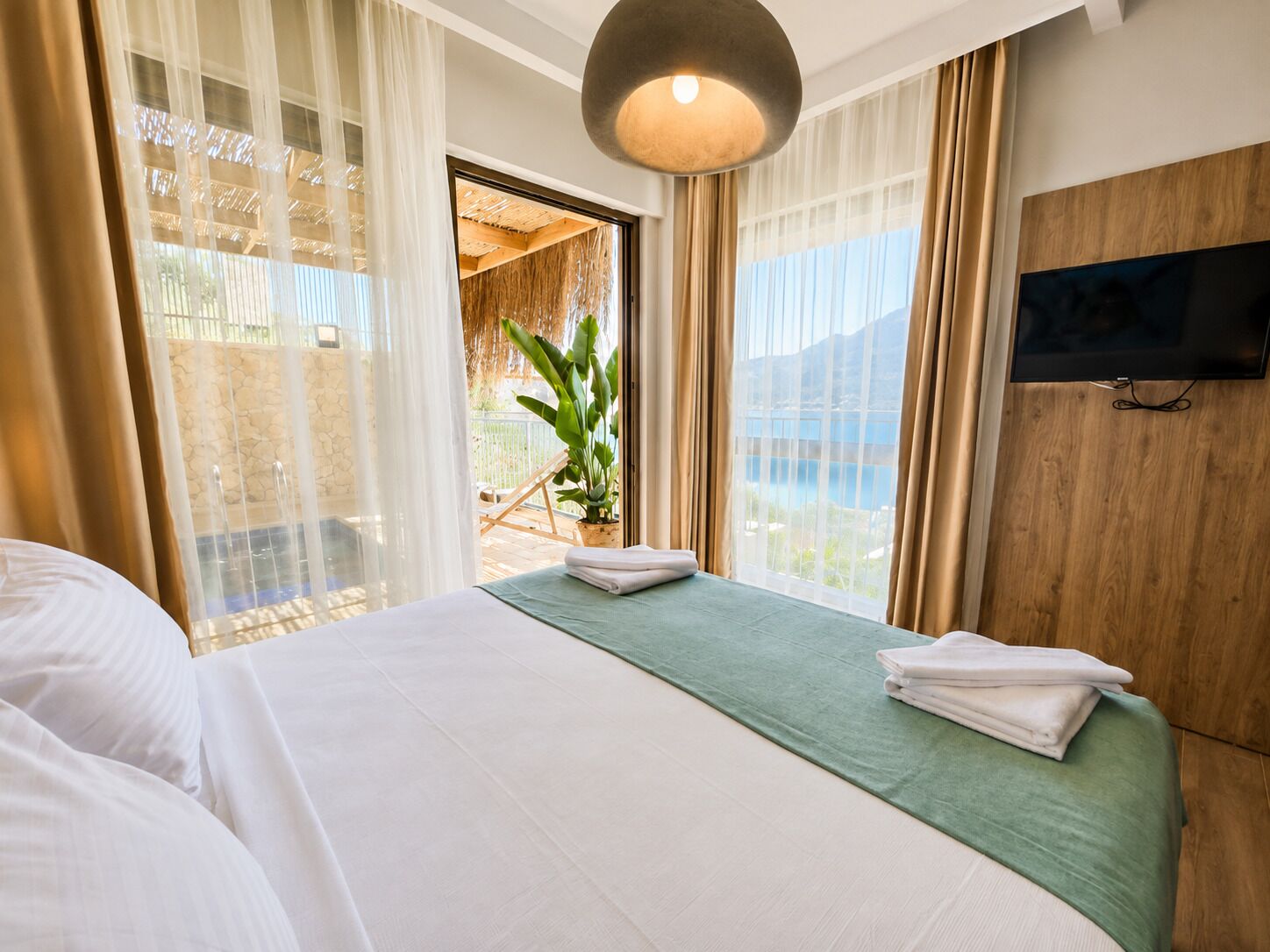 A hotel room with a bed, a television, and a view of a pool and mountains.