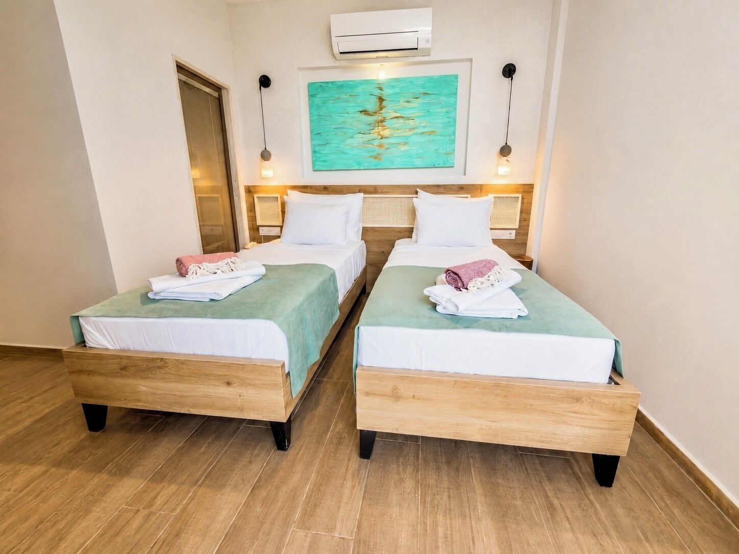 Une chambre d’hôtel avec deux lits en bois, un tableau au mur et un appareil de climatisation.