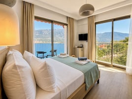 A hotel room with a bed, a desk, a chair, a TV, and a balcony with a view of the mountains.