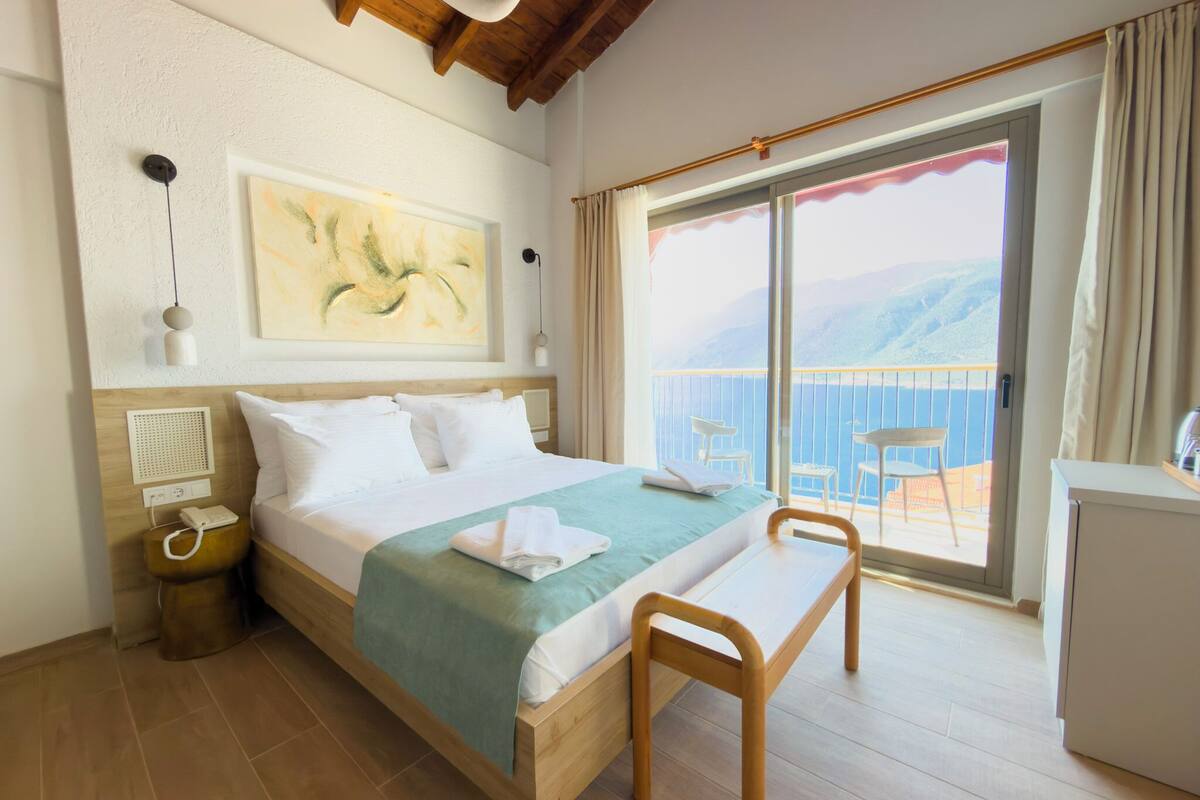 Habitación de hotel con cama, mesita de noche, lámpara, obra de arte y balcón con vistas.