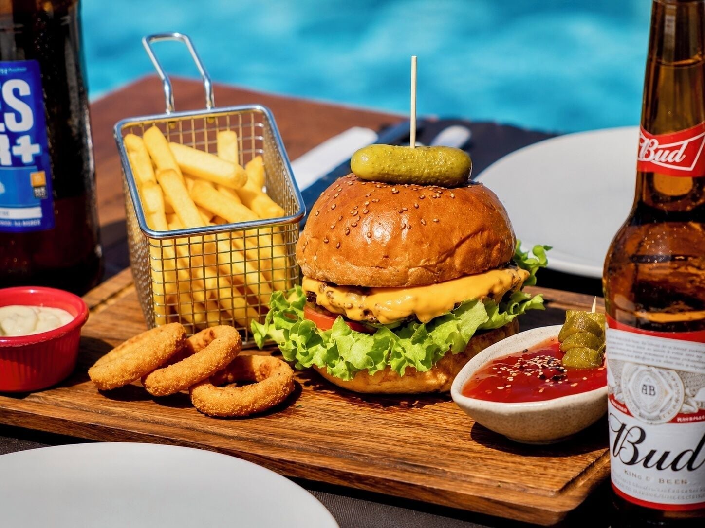A meal with a burger, fries, onion rings, and a bottle of beer.