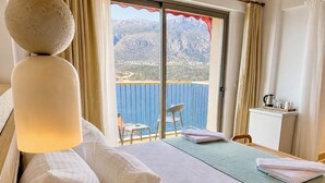 A hotel room with a bed, a small table, a chair, a desk, and a view of the sea and mountains. - Adasya Hotel (Kas)