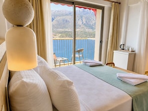 Habitación de hotel con cama, una mesita, una silla, un escritorio y vistas al mar y a las montañas.