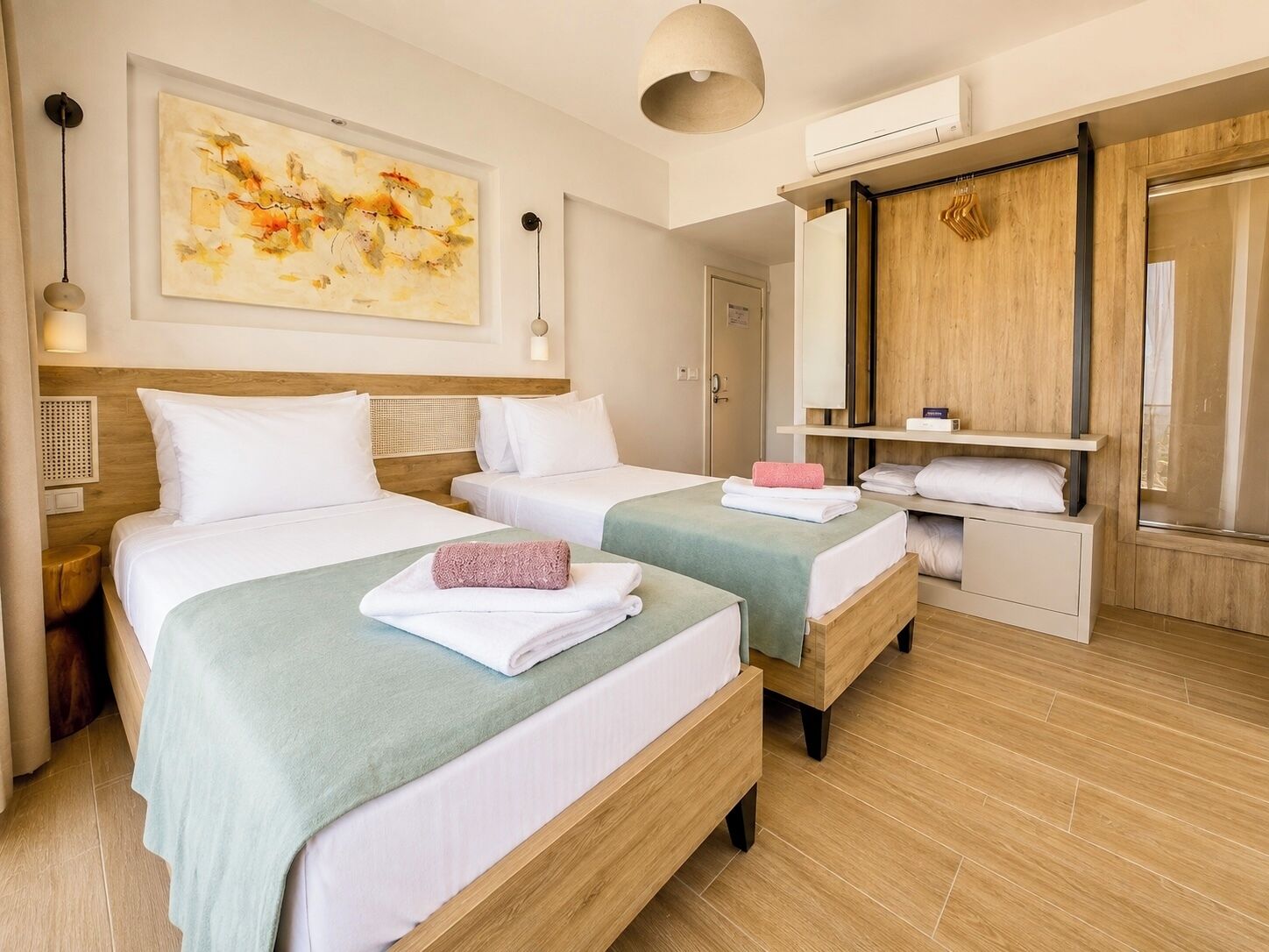 Una camera d'albergo con due letti, un quadro astratto di grandi dimensioni, un armadio in legno e uno specchio.