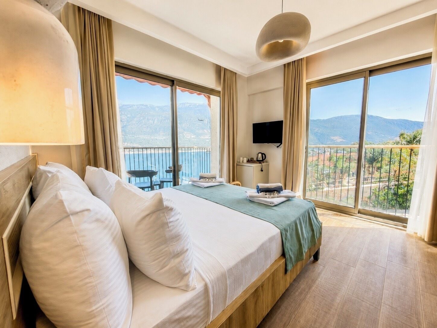 A hotel room with a bed, a TV, a balcony with a view, and a table with chairs.