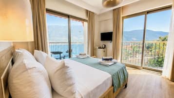 A hotel room with a bed, a TV, a balcony with a view, and a table with chairs.