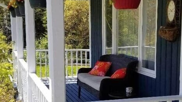 En inglasad veranda med ett vitt räcke, en bänk och hängande blomkorgar.