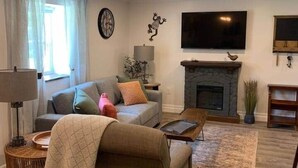 A living room with a sofa, armchair, TV, fireplace, and a clock on the wall. - The Trinity Guest Suite, Trinity Guest House (Trinity)