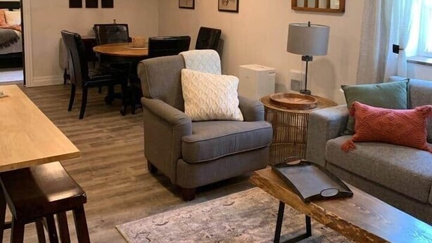 A living room with a sofa, armchair, and coffee table, a dining area with a table and chairs, and a chandelier. - The Trinity Guest Suite, Trinity Guest House (Trinity)