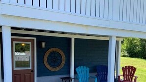 A two-story building with a covered porch, a wooden door, and a small table. - The Trinity Guest Suite, Trinity Guest House (Trinity)