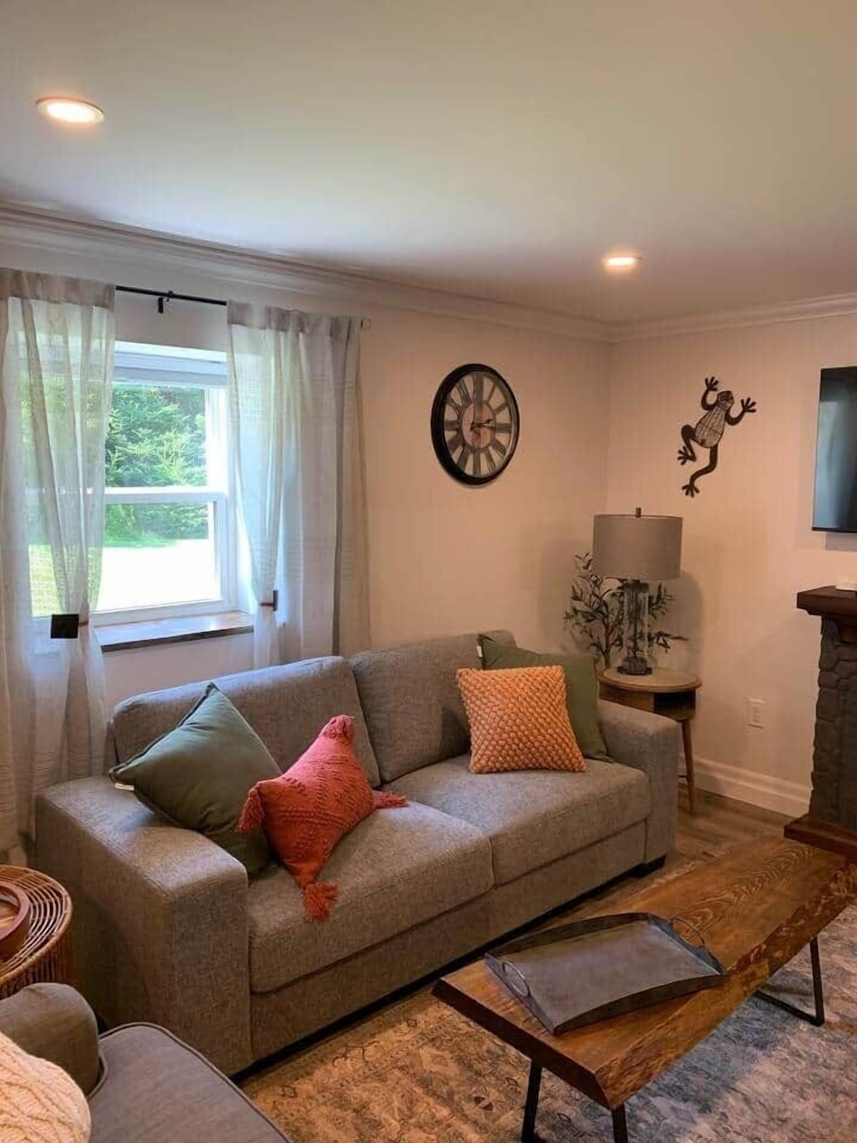 A living room with a grey sofa, a wooden coffee table, a lamp, and a wall clock.