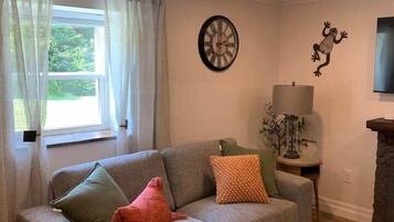 A living room with a grey sofa, a wooden coffee table, a lamp, and a wall clock.