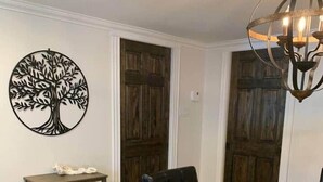A dining area with a round wooden table, black upholstered chairs, a chandelier, and a wall-mounted tree artwork. - The Trinity Guest Suite, Trinity Guest House (Trinity)