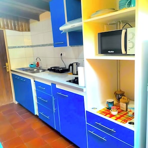 Une cuisine compacte avec des meubles bleus, un four à micro-ondes et un petit plan de travail comprenant une bouilloire et une machine à café.