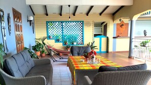 Een terras met wicker meubels, een tafel met een kleurrijke tafelkleed en potplanten.