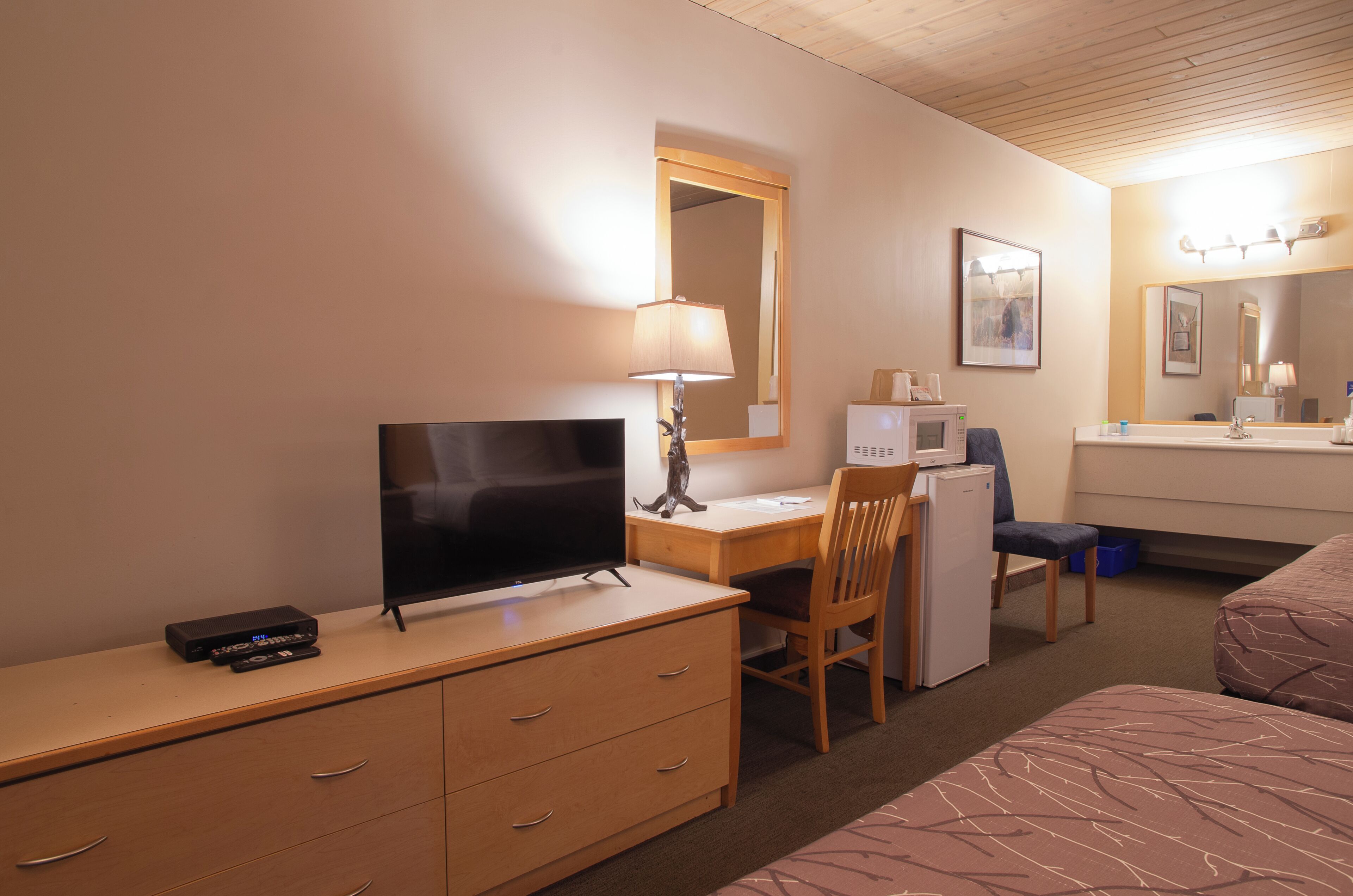 Hotellihuone, jossa on työpöytä, tuoli, televisio ja sänky.