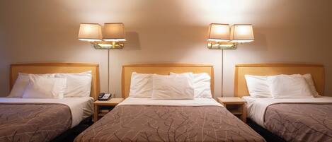 A hotel room with three single beds, each with a wooden headboard, white bedding, and a brown tree branch pattern on the bedspread. There are two wall-mounted lamps on either side of the room.