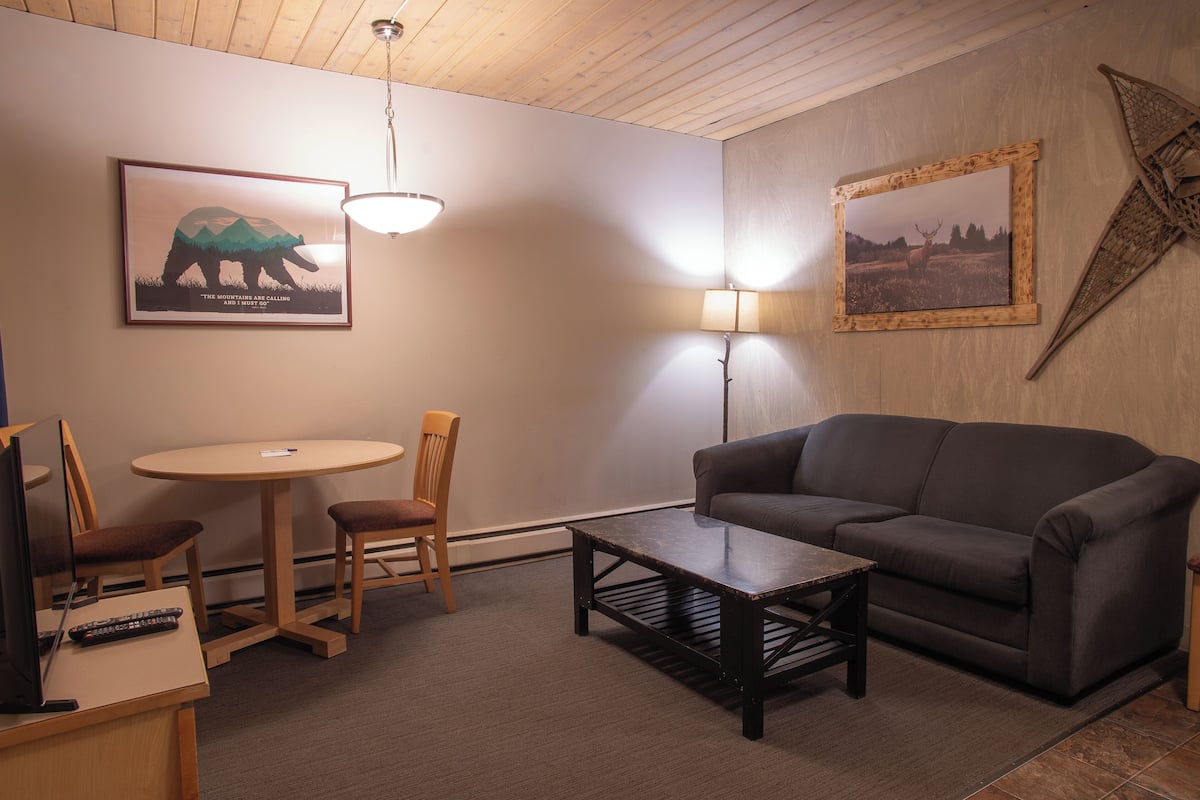 Una sala de estar acogedora con un sofá, una mesa de centro, un televisor y un comedor con sillas y una pequeña mesa.